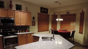 A kitchen with granite countertops, stainless steel appliances, wooden cabinets, and a dining area with a table and chairs.