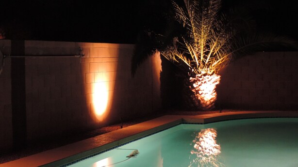 A swimming pool with a tiled edge, a water feature, and a wall with a light fixture.