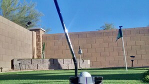 A golf course with a clear sky, a well-maintained lawn, and a brick wall in the background.