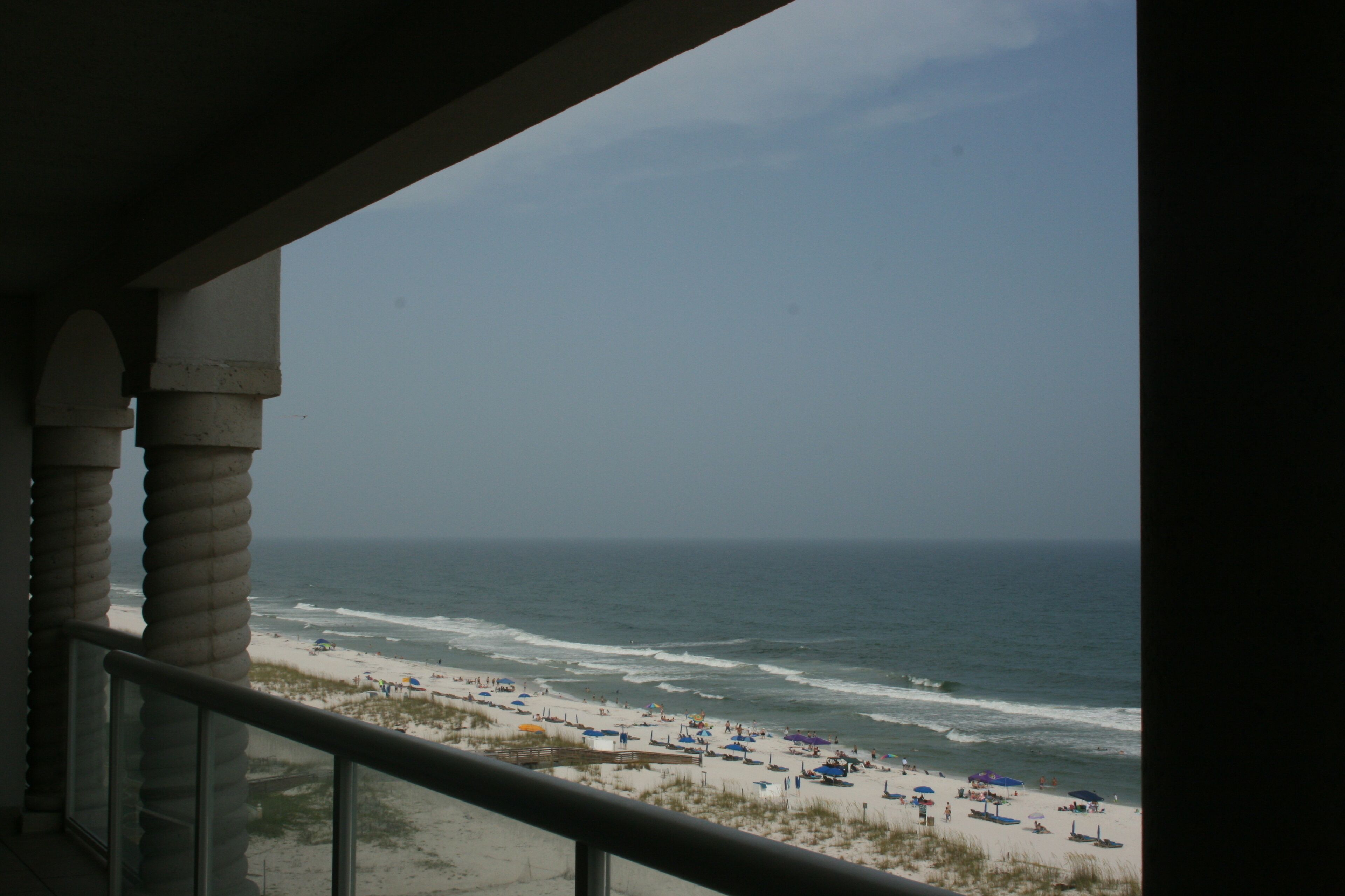 A balcony with a view of a beach with umbrellas and people.