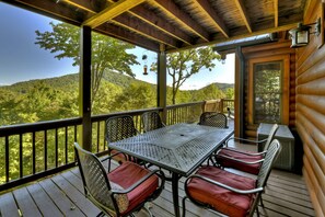 A covered outdoor deck with a table and chairs, overlooking a forested hillside.