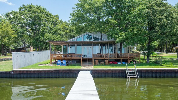 A house with a dock extending into a pond, surrounded by trees and a grassy area.