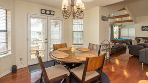 A dining area with a round table, chairs, and a chandelier. There is a pool table in the background.