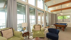 A spacious room with large windows, a pool table, and two armchairs.