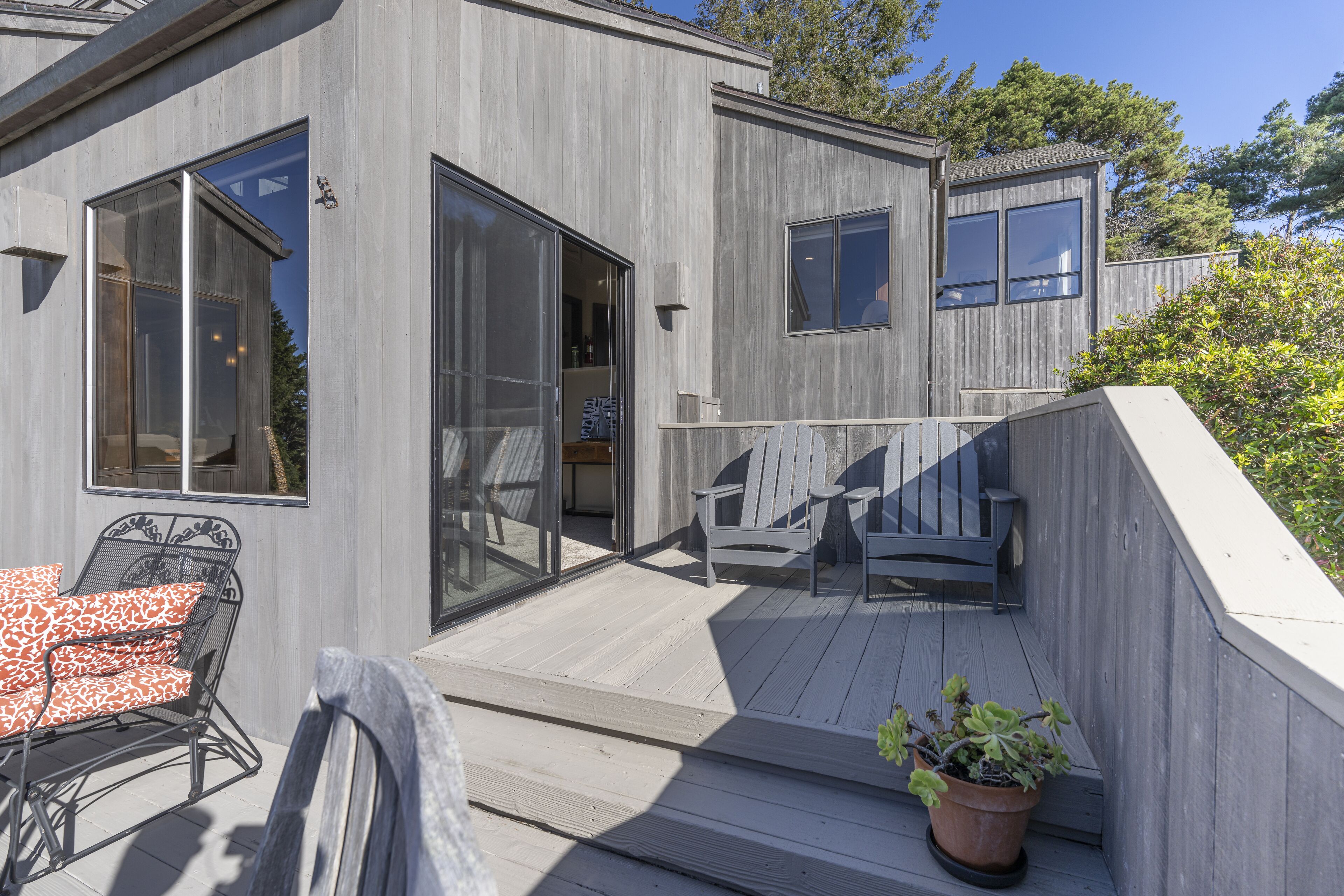 Un bâtiment moderne doté d’une terrasse en bois, de grandes fenêtres et d’un espace salon extérieur.