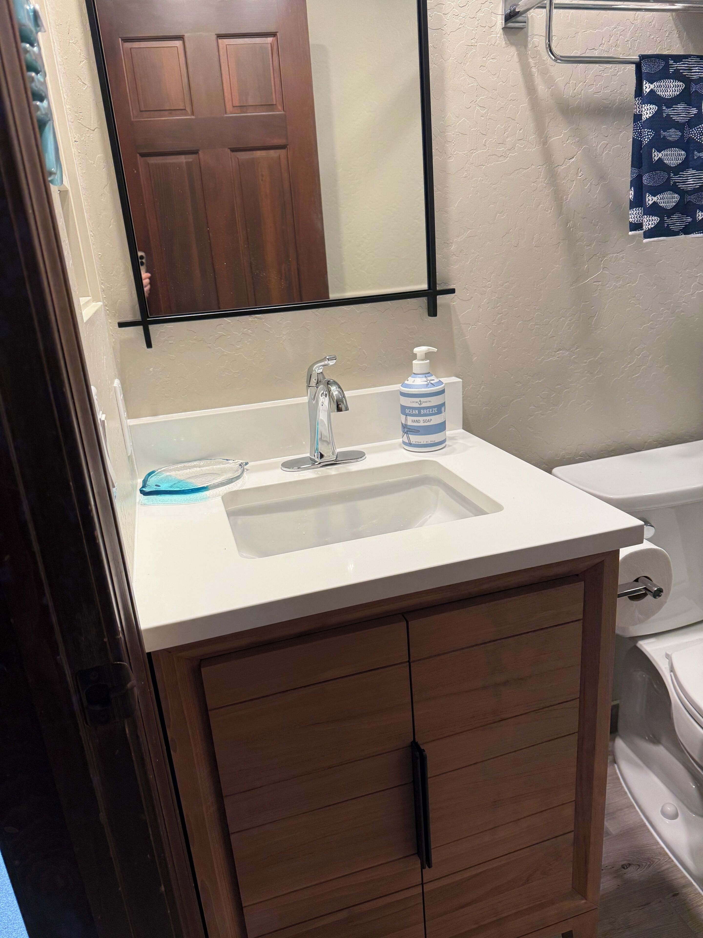 A bathroom with a white sink, wooden cabinet, and a mirror above the sink.