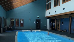 Ein Innenpool mit klarem, blauem Wasser, Holzbalkendecke und einer blauen Wand mit Fenstern.
