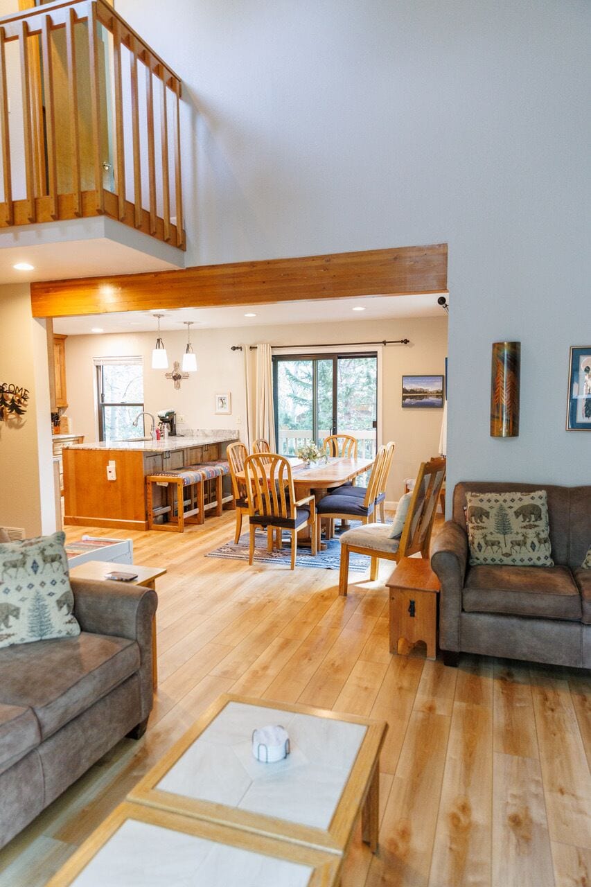 A spacious living area with a wooden floor, a dining table with chairs, a sofa, and a staircase.