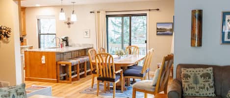 A spacious living area with a wooden floor, a dining table with chairs, a sofa, and a staircase.