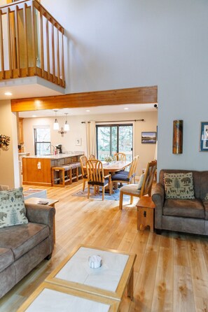 Un espacio habitable amplio con suelo de madera, una mesa de comedor con sillas, un sofá y una escalera.