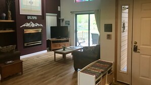 Ein Wohnzimmer mit Fernseher, Kamin und Blick ins Freie.