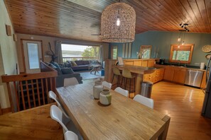 Una mesa de comedor de madera con sillas y una lámpara colgante en una habitación con vistas al exterior.