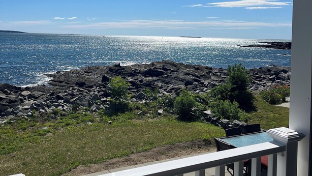 Een balkon met uitzicht op de oceaan, een rotsachtige kustlijn en een helderblauwe lucht.