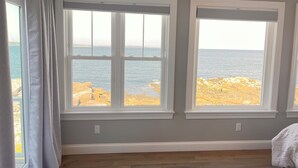 A room with two large windows overlooking a rocky coastline.