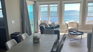 A spacious room with a long dining table, several chairs, a sofa, and a chair with a view of the sea. - Amazing Oceanfront  Brand NewHome Ideal location - (Portland)