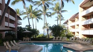 Un espace piscine doté de chaises longues et d’un jacuzzi, entouré de palmiers et bordé d’un bâtiment avec des balcons.