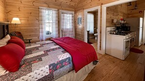A wooden cabin room with a bed, a desk, and a kitchenette. - Osgood Cabin with Lake View (Paul Smiths)