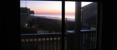 Vista desde una ventana hacia una playa al atardecer.
