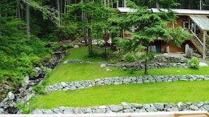 Uma cabana com um muro de arrimo de pedra, gramado e deck de madeira.