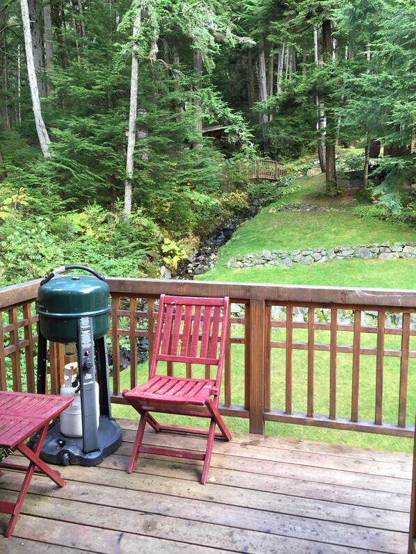 A wooden deck with a grill, a red chair, and a stone wall.