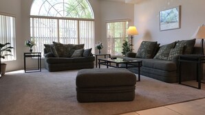 A spacious living room with a large arched window, two sofas, a coffee table, and a floor lamp. - Look at This! Fun in the Sun for Everyone! (Kissimmee)