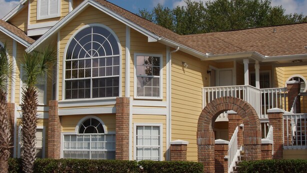 A two-story house with a yellow exterior, a brick archway entrance, and a covered porch with white railings. - Look at This! Fun in the Sun for Everyone! (Kissimmee)