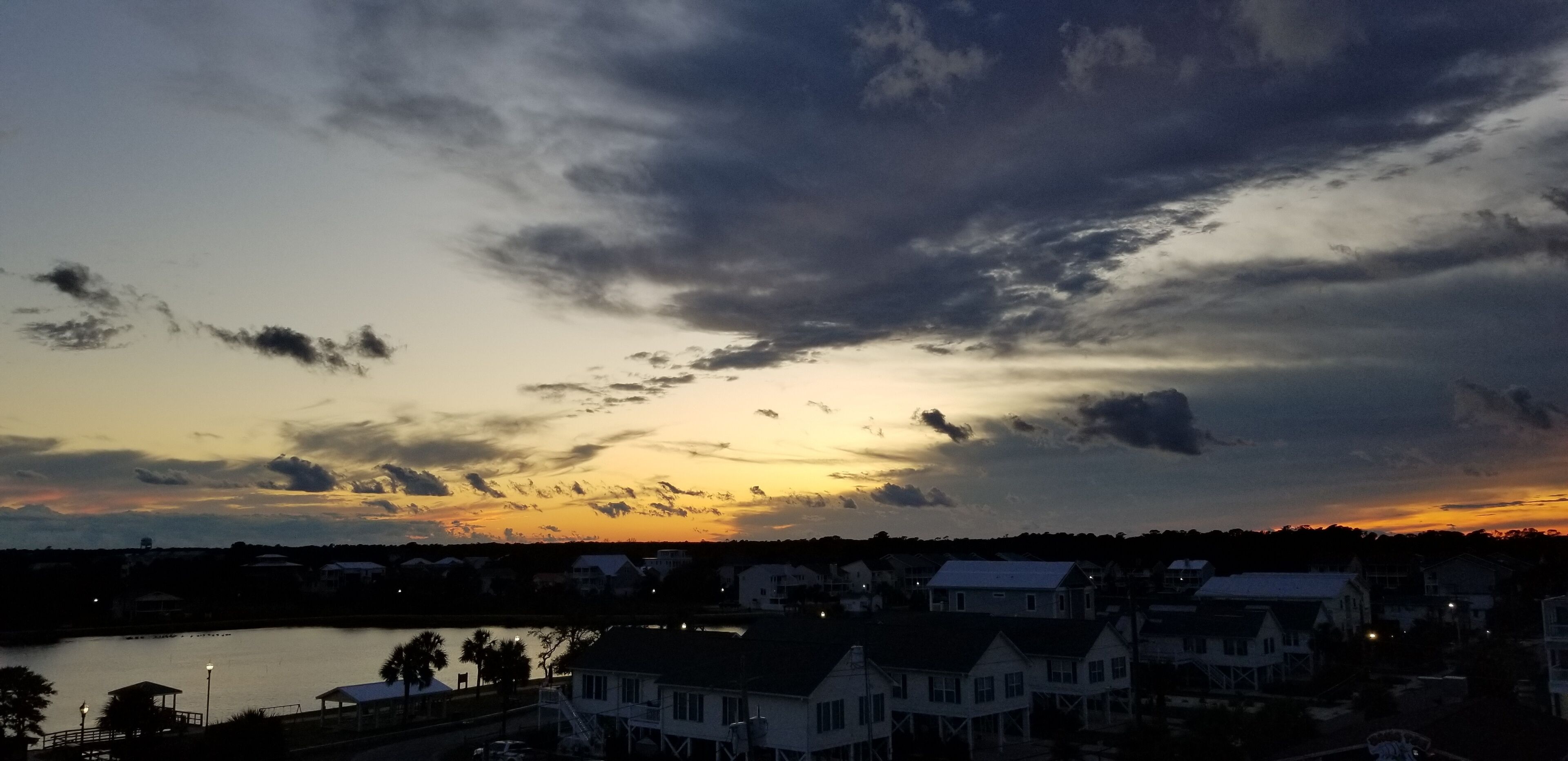 Un atardecer sobre una zona residencial con casas y una masa de agua.