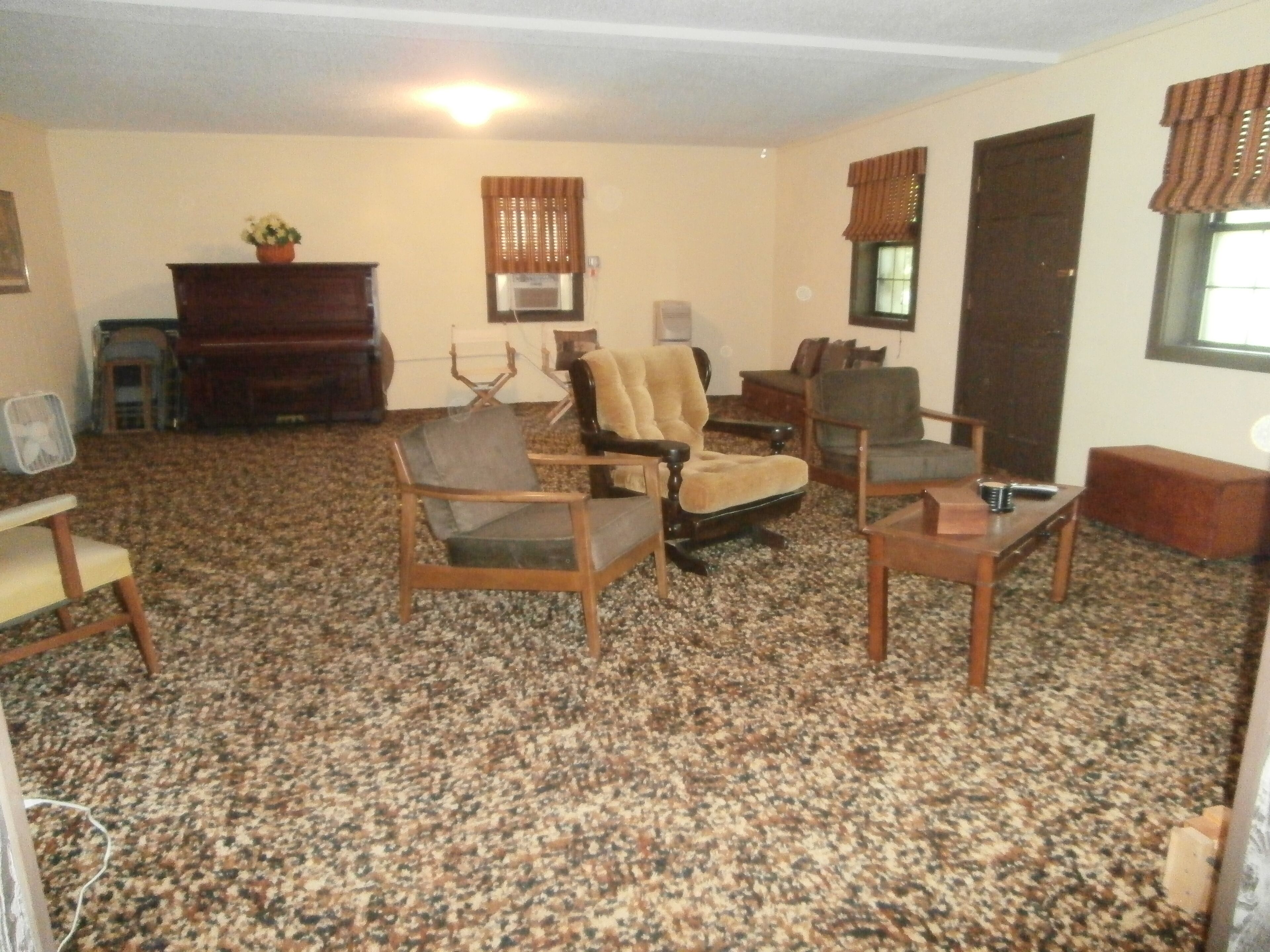 A living room with a carpeted floor, several chairs, a coffee table, a fireplace, and a television.