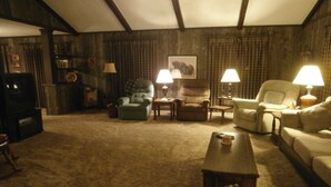 A cozy living room with a high ceiling, a television, and multiple seating options including a sofa, chairs, and a small table.