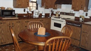 A kitchen with wooden cabinets, a round dining table with chairs, a microwave, a stove, and a coffee maker.