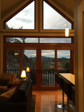En rummelig stue med stor skydedør til en balkon, træloft og spiseområde med bord og stole.