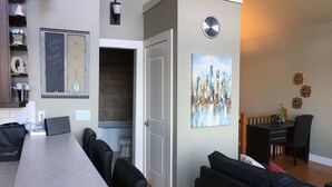 A modern living room with a long dining table, black leather sofas, a cityscape painting, and a clock on the wall. - "Quails Run Retreat" on Bear Mountain  (Victoria)
