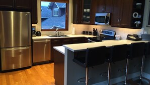 A modern kitchen with stainless steel appliances, wooden cabinets, and a large island with bar stools. - "Quails Run Retreat" on Bear Mountain  (Victoria)