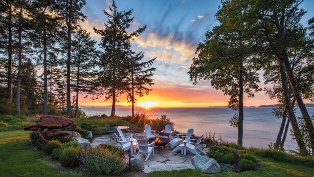 A patio with Adirondack chairs and a fire pit overlooking a lake at sunset. - Orcas Waterfront Custom Home, 180 Degree Summer Sunset & Sunrise,  Sleeps 12 (Eastsound)