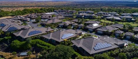 A residential area with houses featuring solar panels, surrounded by greenery and a mountain in the background.