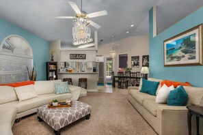 A spacious living room with a high ceiling, a chandelier, and a dining area with a kitchen in the background. - Heated Pool! 5 Minute Bike To Beach, Dining, Mercato! Bikes Included (Naples)