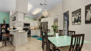 Una cucina moderna con mobili bianchi, un'isola centrale e un'area pranzo con tavolo in vetro e sedie in legno.