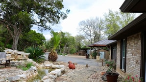 A stone pathway leading to a house with a brick exterior, a small pond, and a bench. - Resort Quality 4B Home With Private Pool In Beautiful Hill Country (New Braunfels)