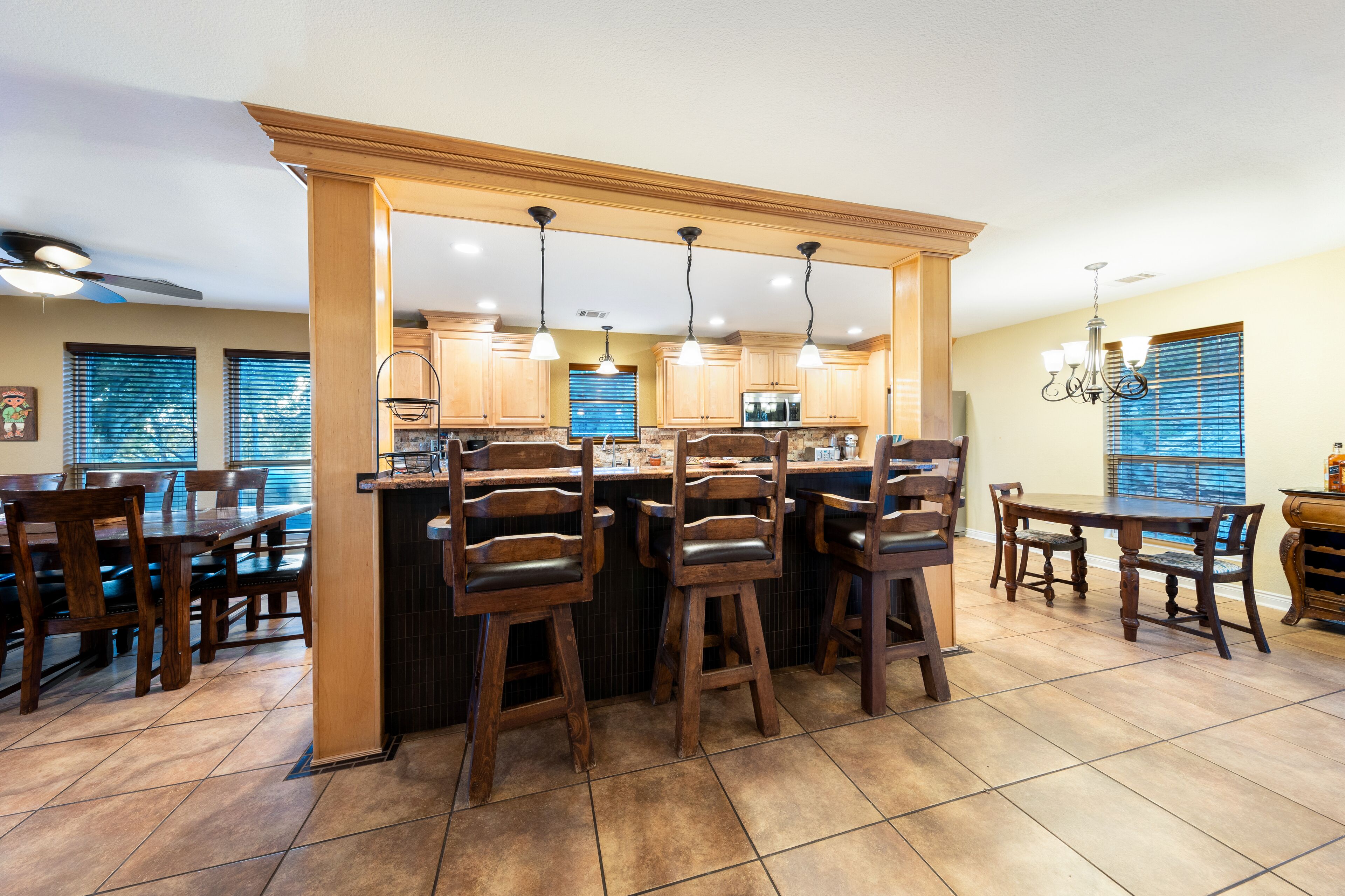 Une cuisine avec des meubles en bois, un îlot central doté de tabourets et un éclairage suspendu.