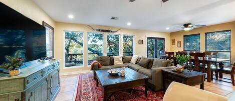 A spacious living room with a large flat-screen TV, a wooden coffee table, a beige sofa, and a red patterned rug.