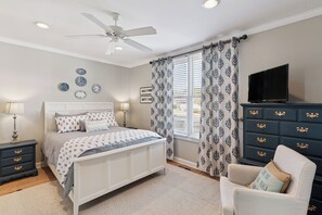 A bedroom with a bed, nightstands, a dresser, a chair, a television, and a ceiling fan.