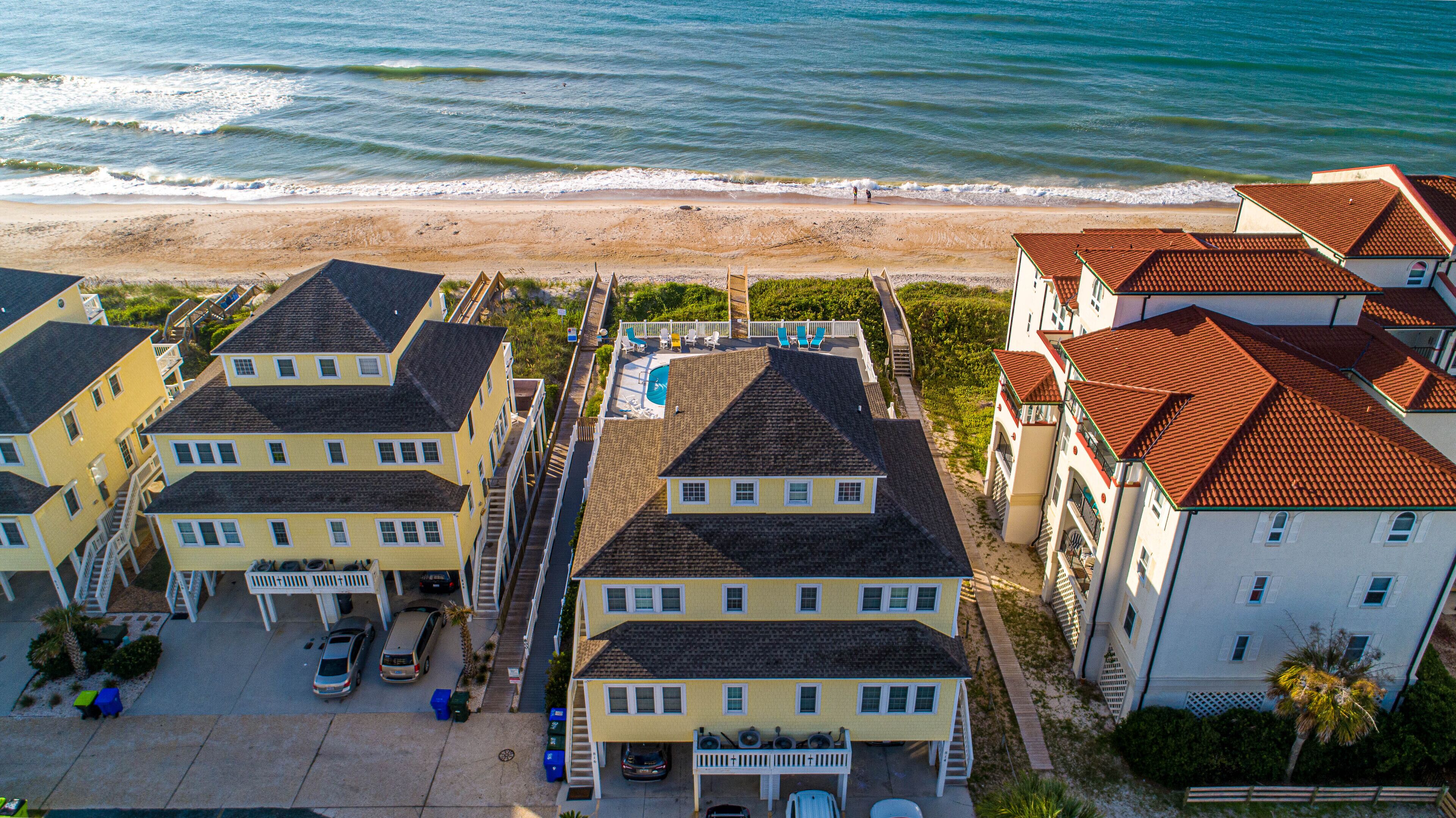 Un quartier résidentiel situé sur la côte, composé de plusieurs immeubles à deux étages, d’une piscine et d’une plage en arrière-plan.