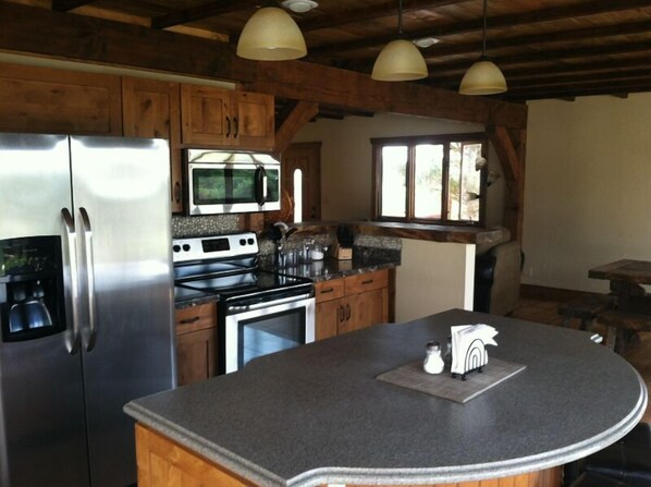 A kitchen with wooden cabinets, a stainless steel refrigerator, a microwave, a stove, and a large island with a mat.
