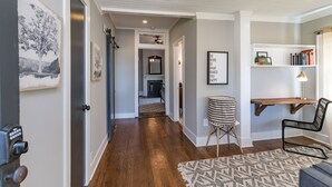 A hallway with hardwood flooring, a patterned rug, a desk with a chair, and a bookshelf. - The Peachtree House  (Nashville)