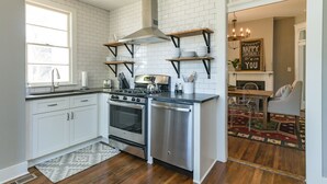A modern kitchen with white cabinets, stainless steel appliances, and wooden shelves above the counter. - The Peachtree House  (Nashville)