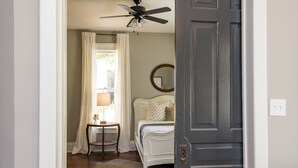 A hallway with a dark wooden door, a ceiling fan, and a bed with white bedding in the background. - The Peachtree House  (Nashville)