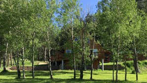 A wooden cabin with a deck, surrounded by a grassy area and trees.