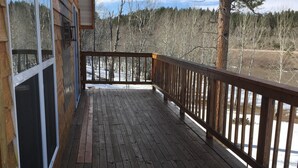 A wooden deck with a railing, overlooking a snowy landscape with trees.