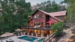 A two-story log cabin with a swimming pool, outdoor seating, and a stone pathway.