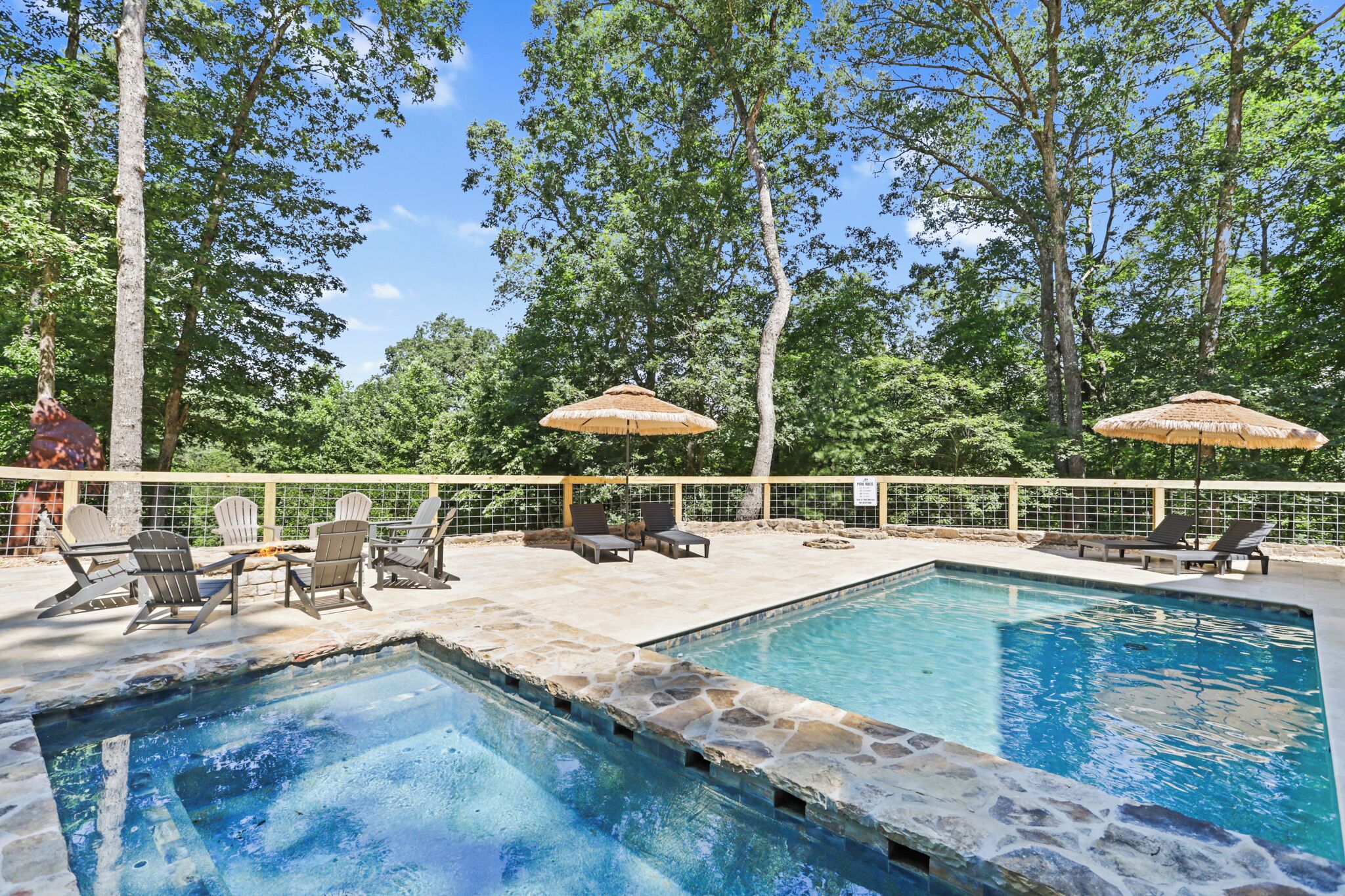 A pool area with lounge chairs and umbrellas, surrounded by trees.
